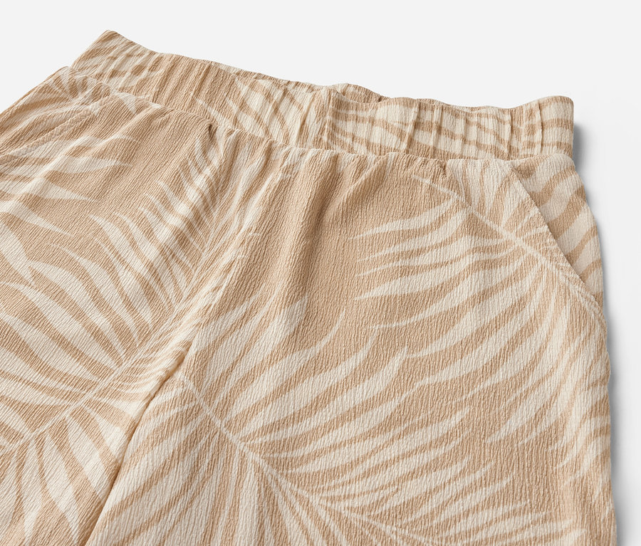 Egy nyomott mintás, strukturált anyagú bőszárú nadrág részlete.