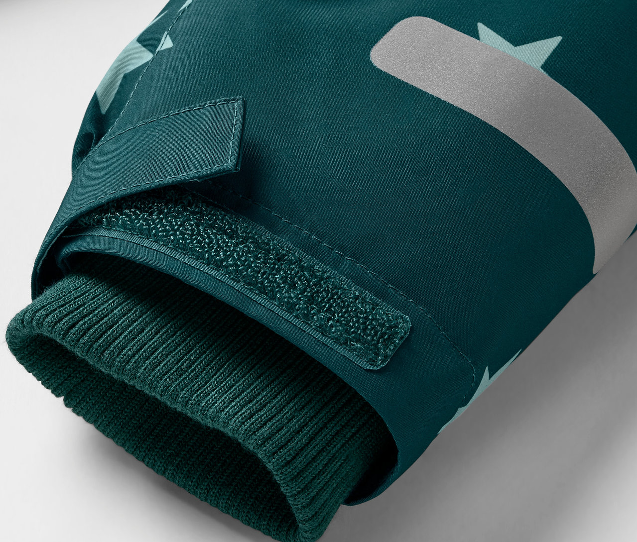 Egy sötétzöld kabát részlete kötött mandzsettával és fényvisszaverő elemmel.