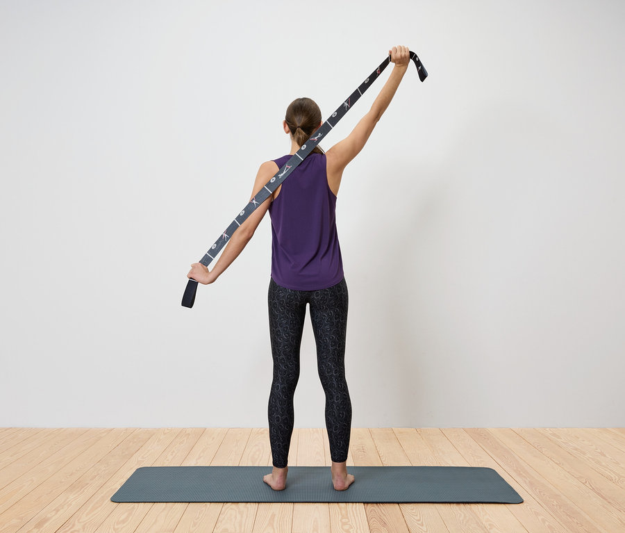 Nő nyújtja a felsőtestét jógaszíjjal.