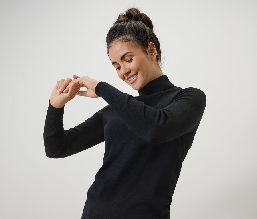 Nő mosolyog és pózol fekete garbóban.