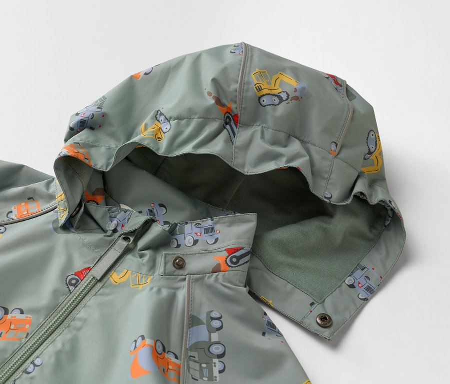 Közelkép egy olívazöld, építőipari teherautókkal nyomott, kapucnis gyerekdzsekiről.