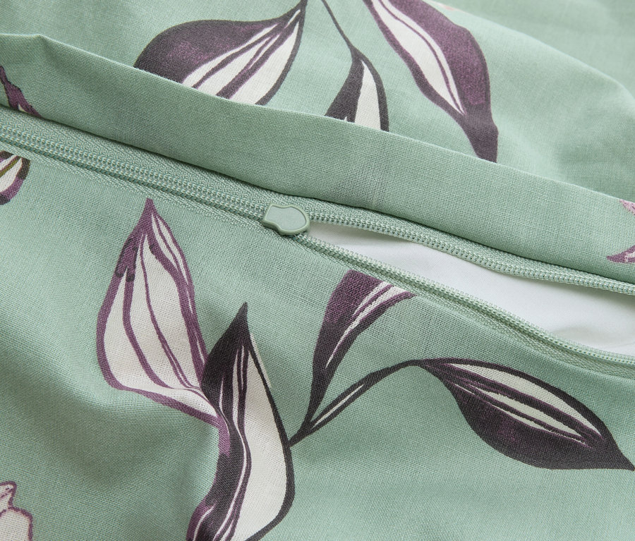 Egy mentazöld színű, cipzáras párnahuzat közeli képe lila levélmintával.