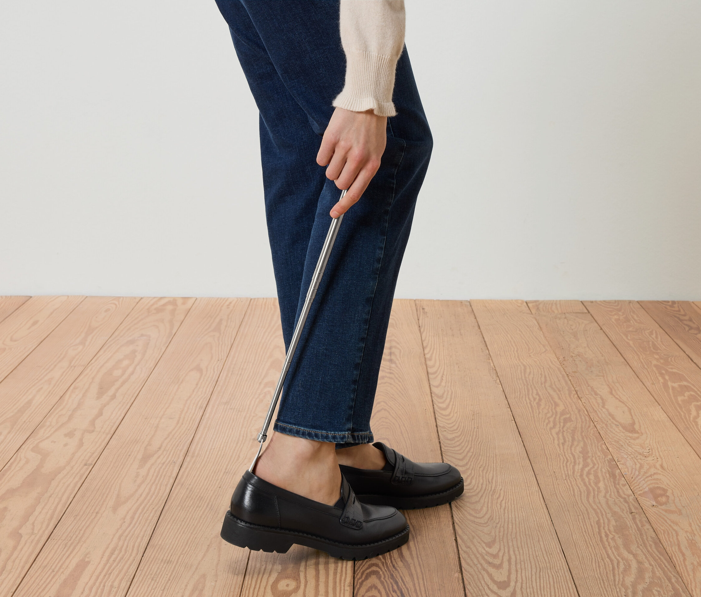 Egy személy fekete loafereket húz fel egy cipőkanállal.