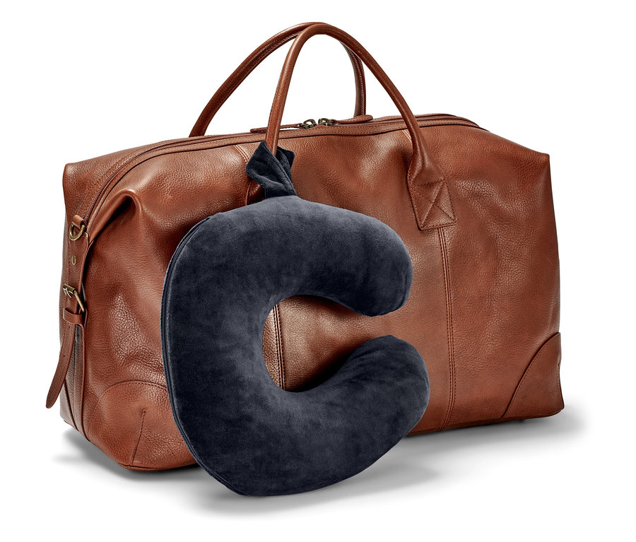 Egy sötétkék nyakpárna lóg egy barna utazótáska előtt.