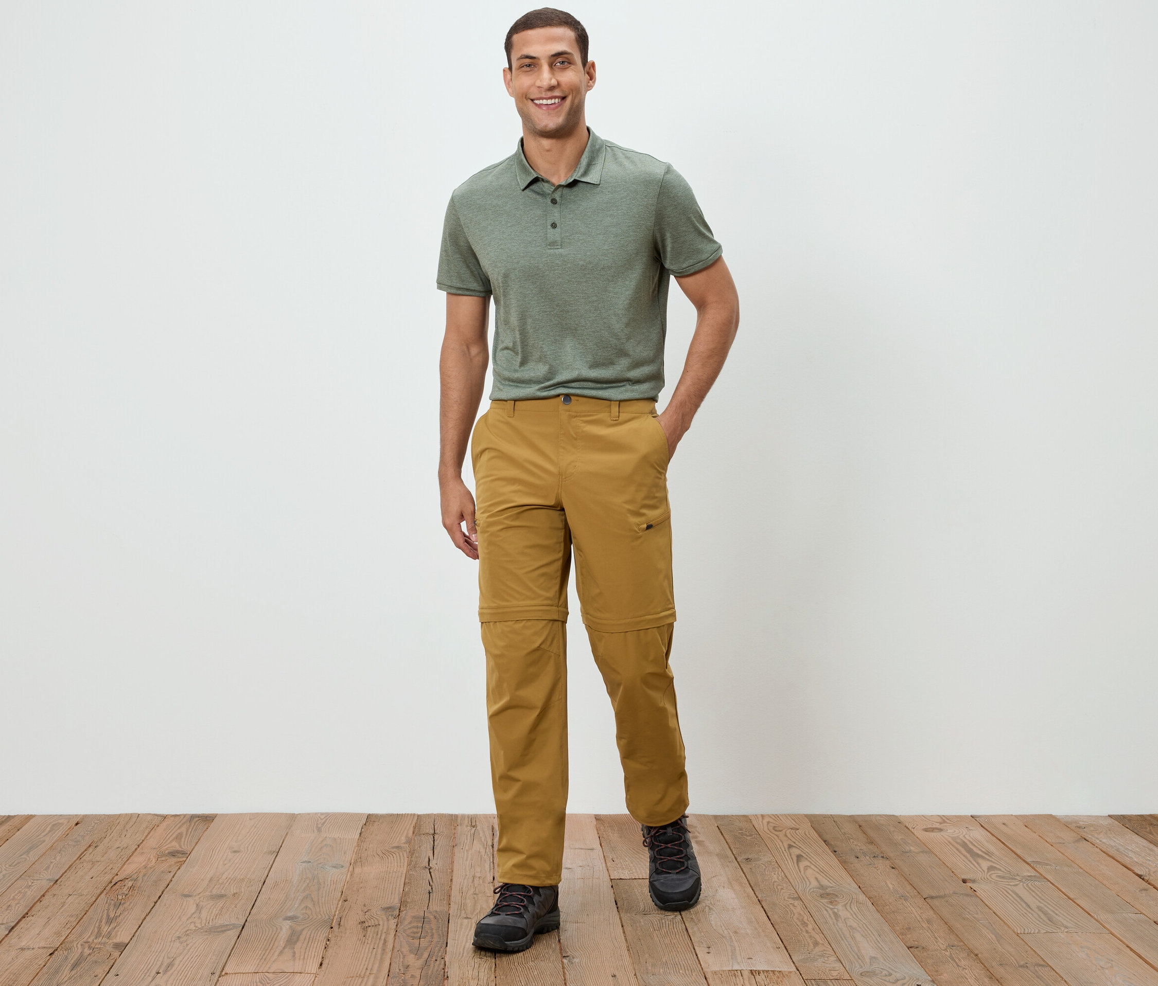 Egy férfi áll egy fehér fal előtt, zöld pólóinget és khaki nadrágot visel.