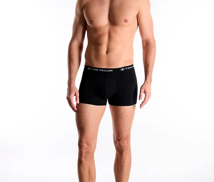 Egy mosolygó férfi fekete TomTailor „Buffer” boxeralsót visel TomTailor felirattal a derékpántján, és lefelé néz.