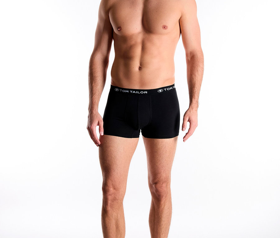 Egy férfi áll mezítláb, és Tom Tailor márkájú fekete boxeralsót visel.