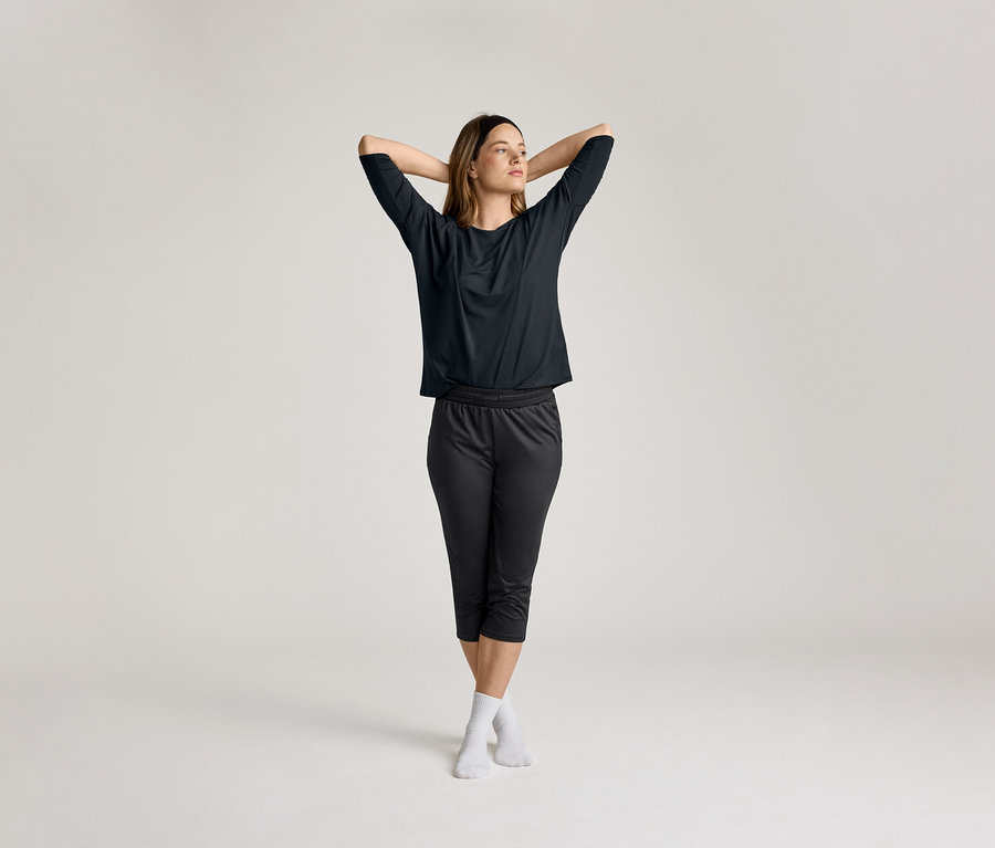 A nő összefonott kézzel a feje mögött fekete 3/4-es sportpólót visel.