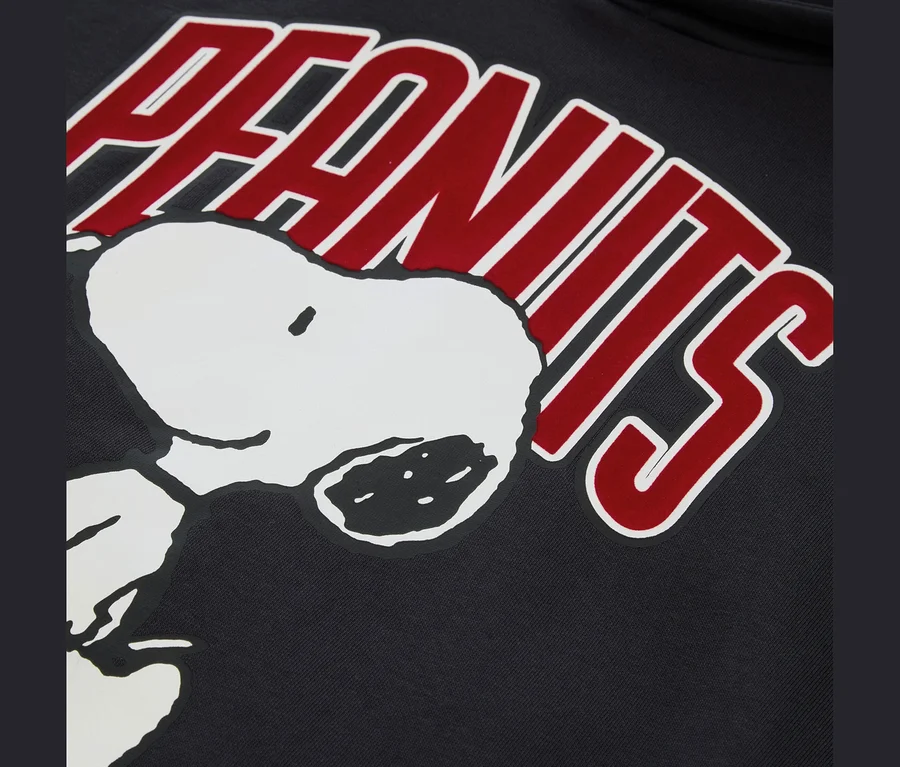 Fekete anyag közeli felvétele, rajta fehér Snoopy fejjel és egy ívelt, piros "PEANUTS" logóval, fehér körvonallal felette.