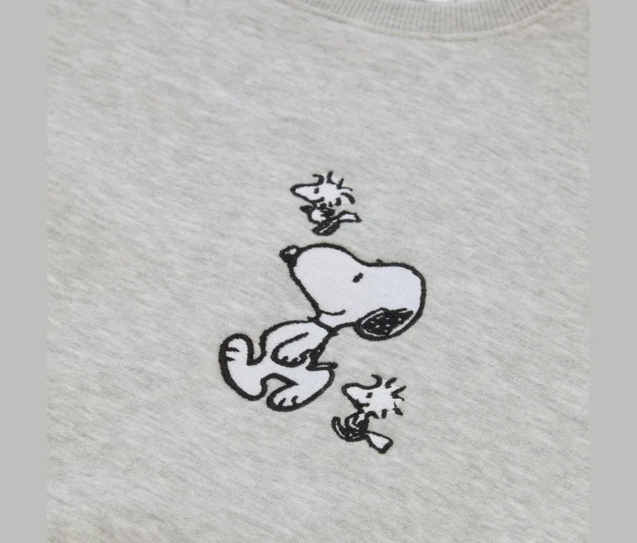 Világosszürke anyag hímzéssel, amelyen Snoopy fekszik a hátán, felfelé nézve, két kis Woodstock figura veszi körül.