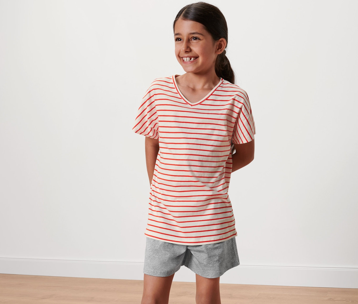 Mosolygó lány piros csíkos, rövidnadrágos pizsamában.