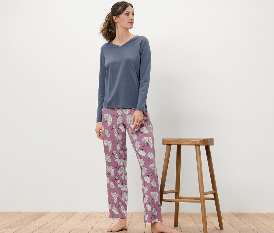 Nő áll egy fa szék mellett, virágos pizsamában.