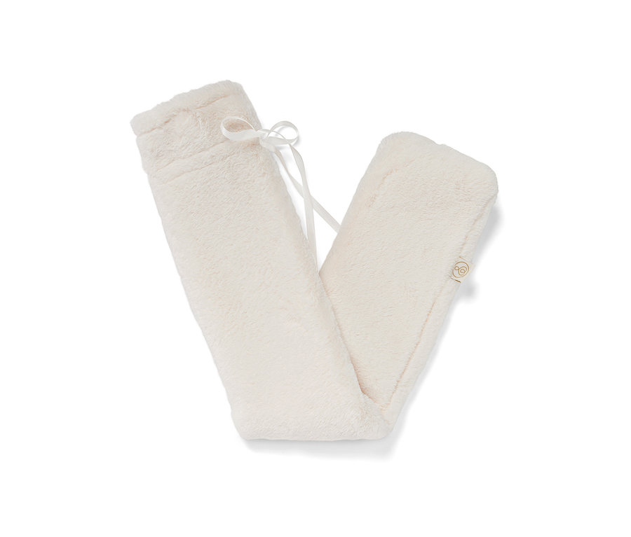 Egy krémszínű, plüss huzatú, tömlő alakú melegvizes palack, fehér szalaggal.