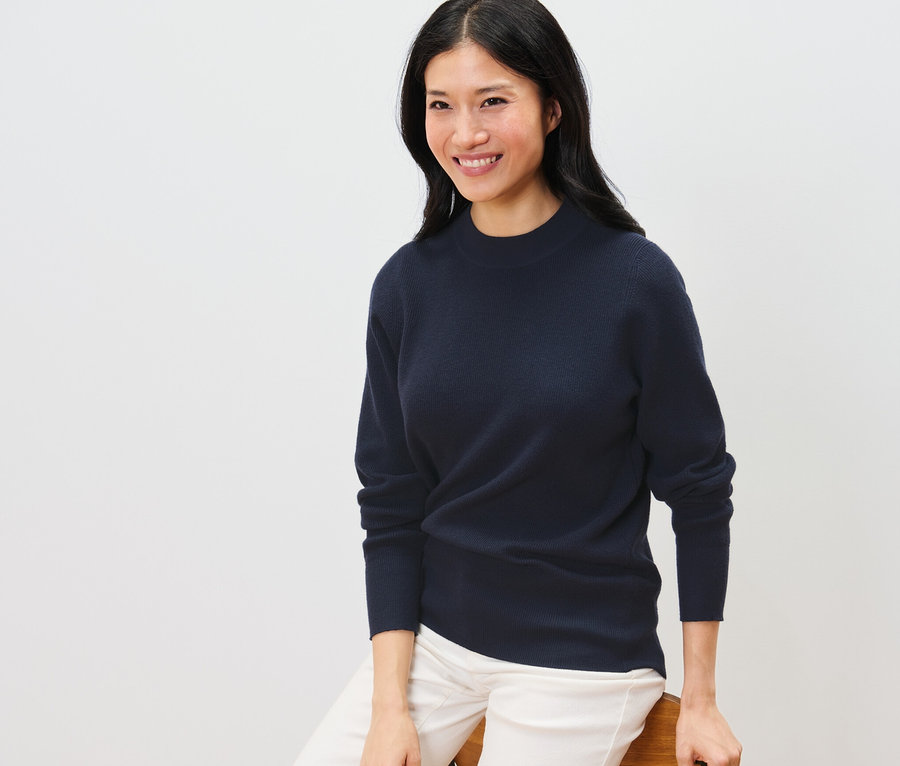 Egy nő ül és sötétkék finomkötésű pulóvert visel.