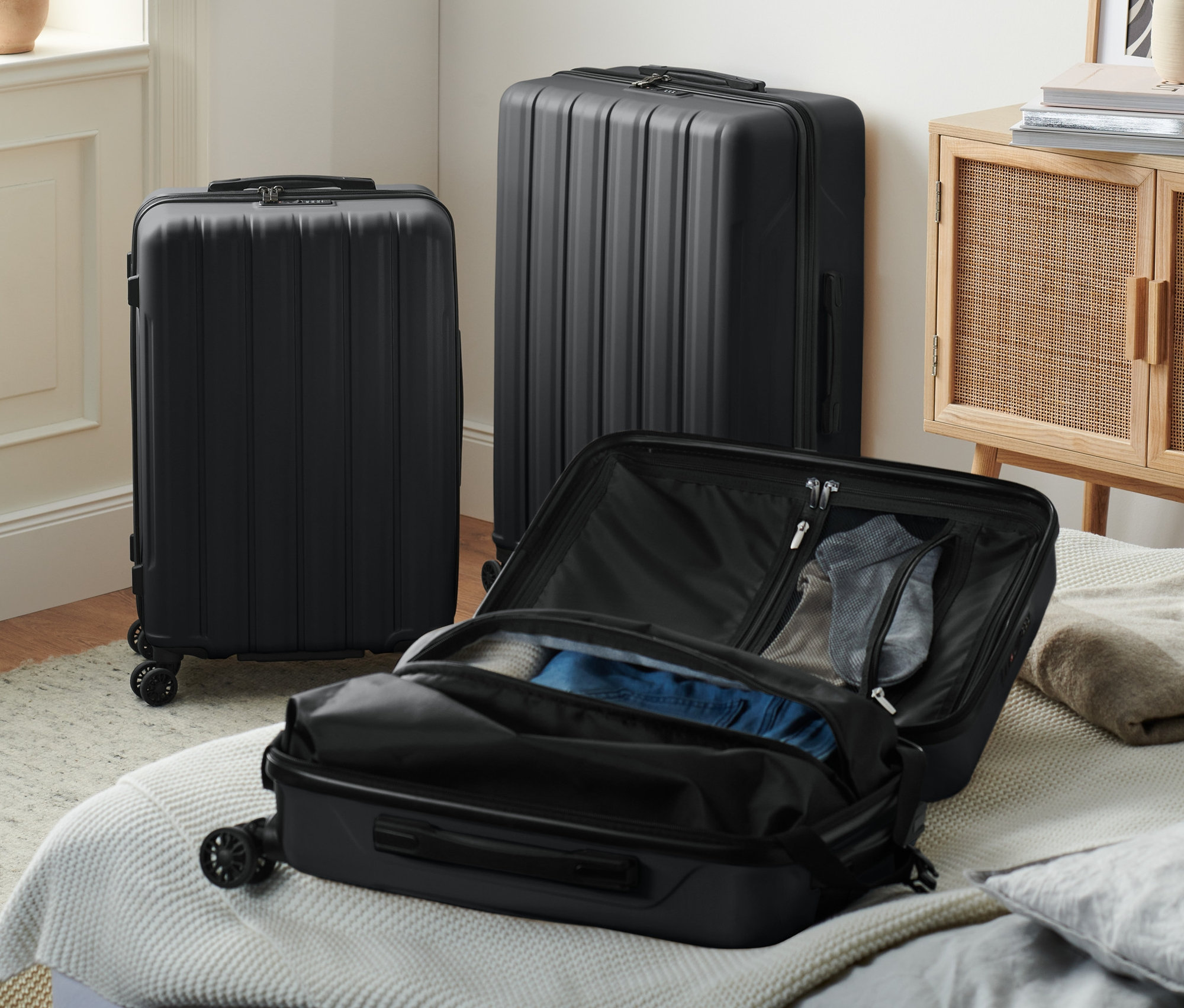 Három fekete kemény bőrönd, egy kicsi nyitva az ágyon.