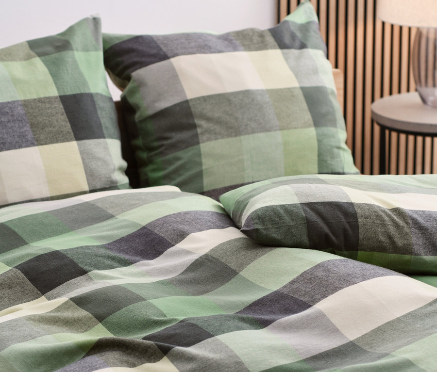 Közelkép egy ágyon lévő zöld, szürke és fehér kockás mintázatú flanel ágyneműről.