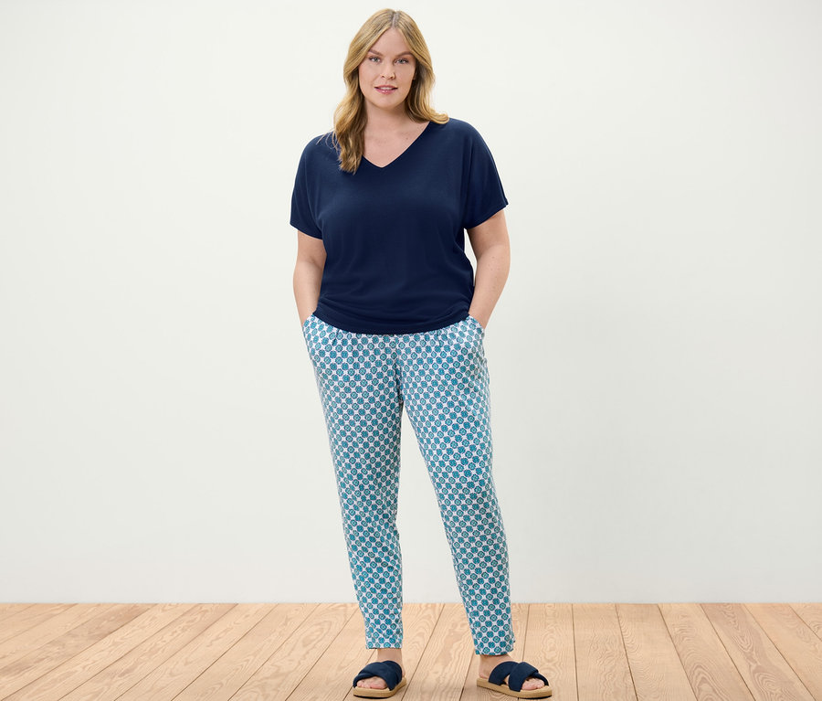 Egy nő áll, sötétkék strukturált felsőt és mintás női jerseynadrágot visel.