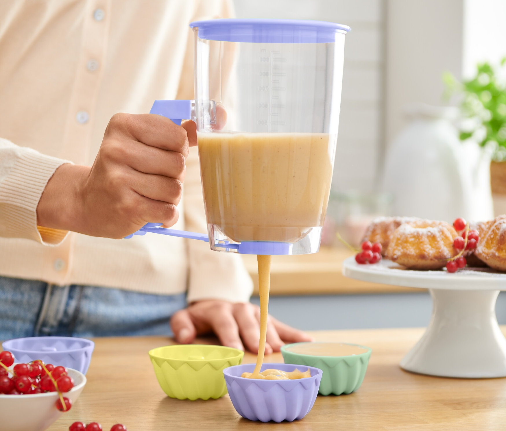Nő adagolja a tésztát a tésztaadagolóval szilikon muffin formákba.