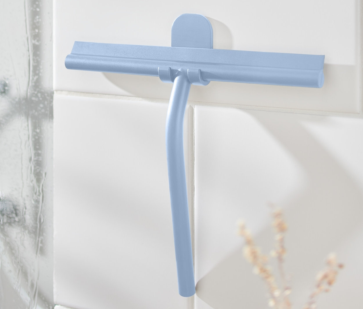 Kék színű vízlehúzó fali tartóval a fehér csempén a zuhany mellett.