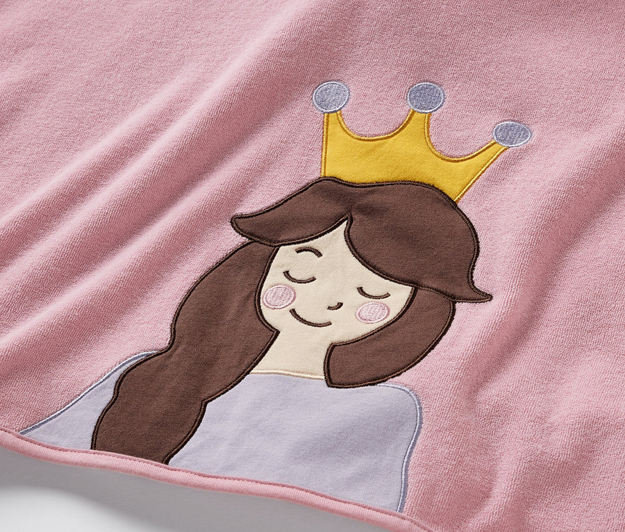 Egy rózsaszín frottír poncsó részlete, hímzett hercegnővel, barna hajjal és arany koronával.