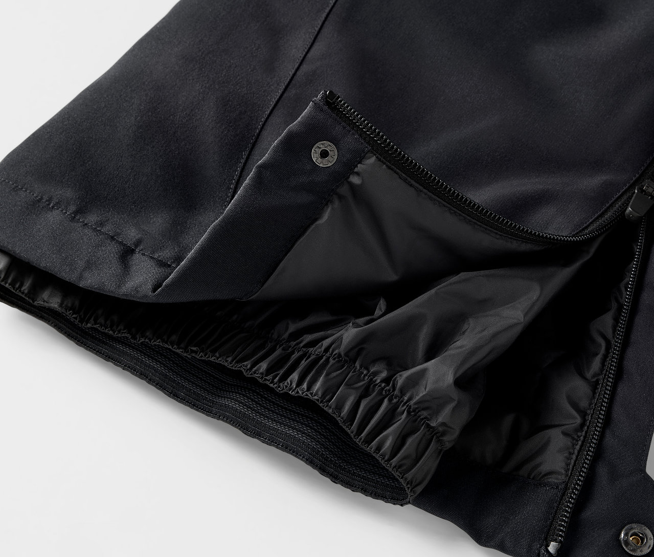 Egy fekete nadrág részlete, nyitott cipzárral és patenttal.