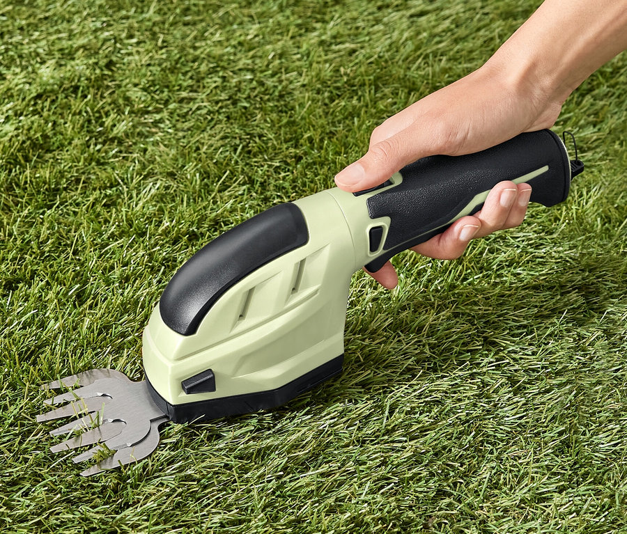 Egy kéz akkumulátoros kerti ollót tart a füvön.
