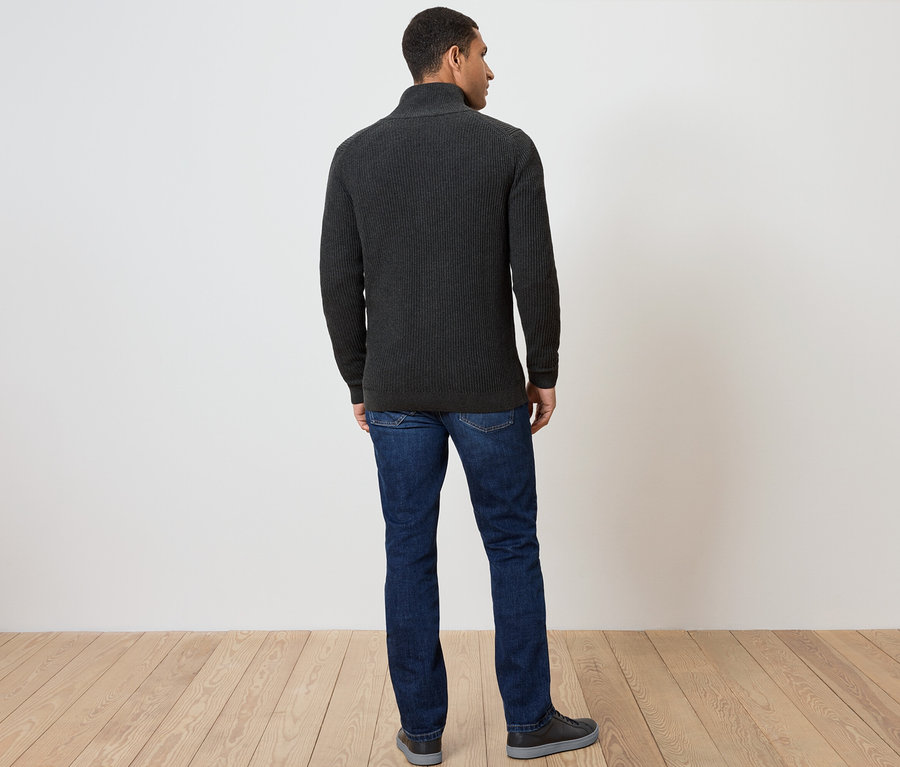 Egy férfi hátulról sötétszürke cipzáras pulóvert, farmert és cipőt visel.