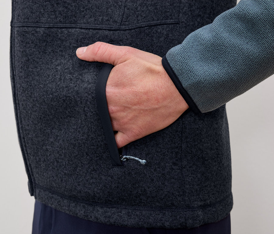 Egy férfi a szürke-kék polárkabátja zsebébe teszi a kezét.