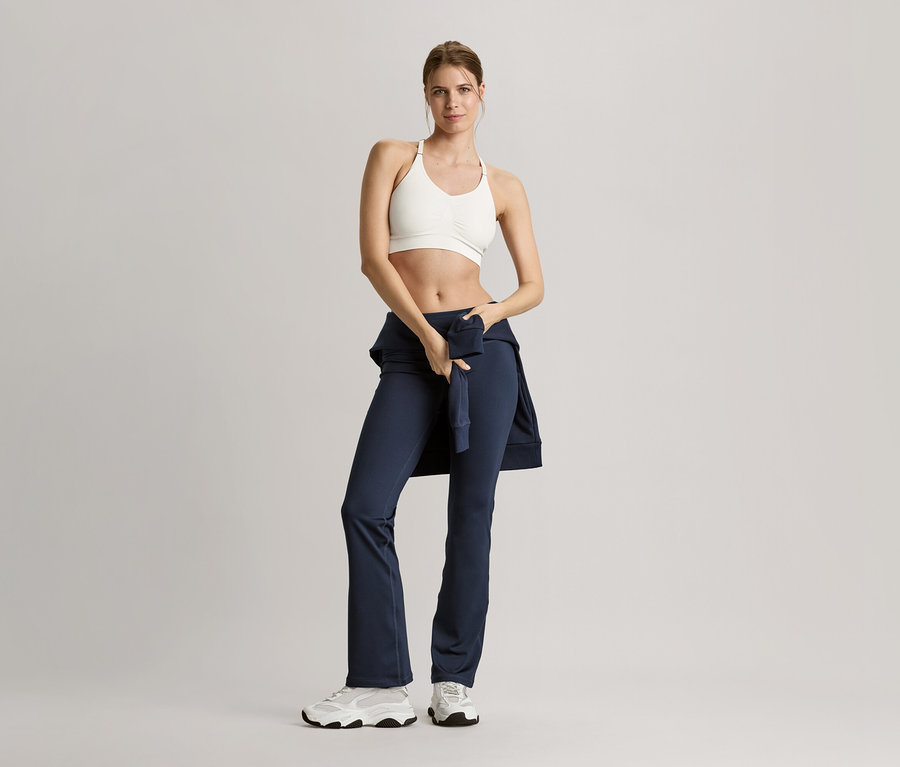 Sportruházatban lévő nő pózol egy tengerészkék szabadidőfelsővel.