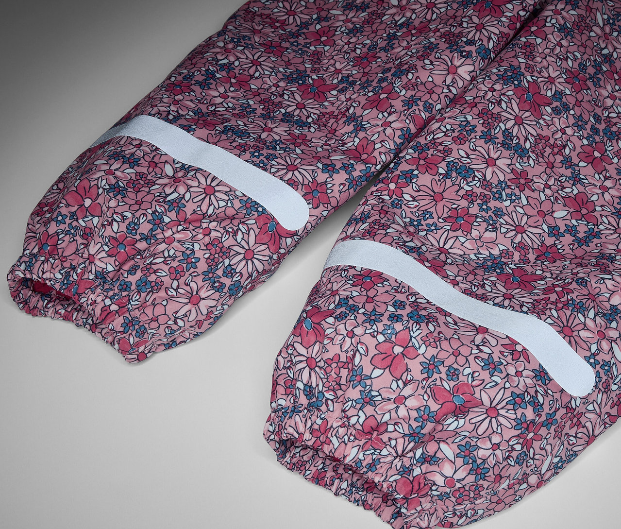 Egy virágmintás, fényvisszaverő csíkokkal ellátott gyerek termo esőnadrág részlete.