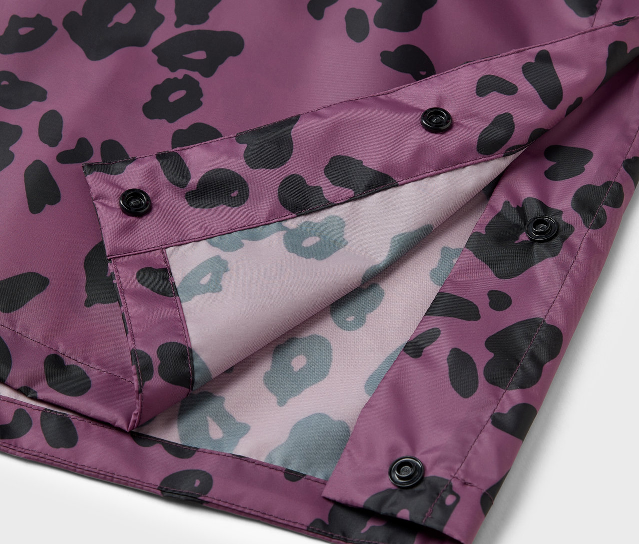 Egy lila kabát részlete fekete állatmintával és fekete gombokkal.