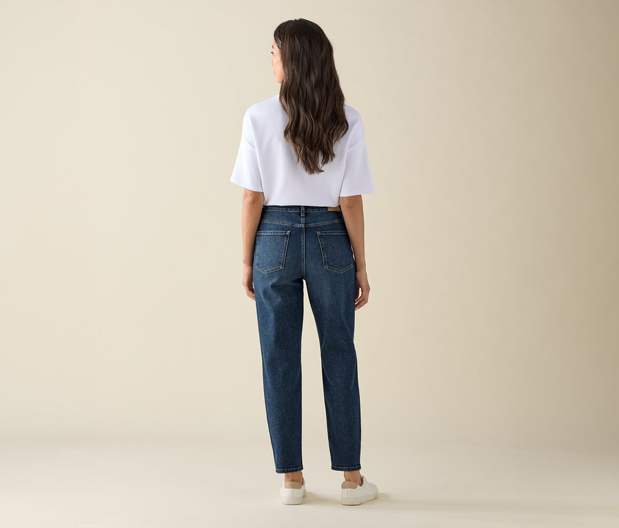 Egy nő áll háttal a kamerának, sötétkék farmernadrágot – »Nyla« fazon – és fehér pólót visel.