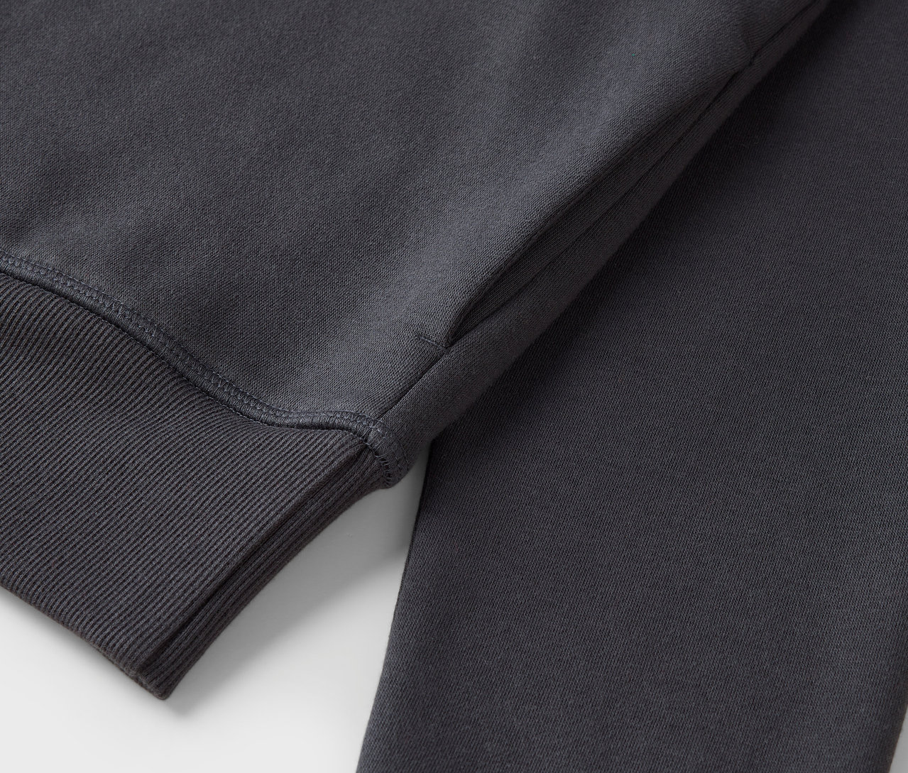 Egy szürke pulóver részlete, bordázott szegéllyel az ujján.