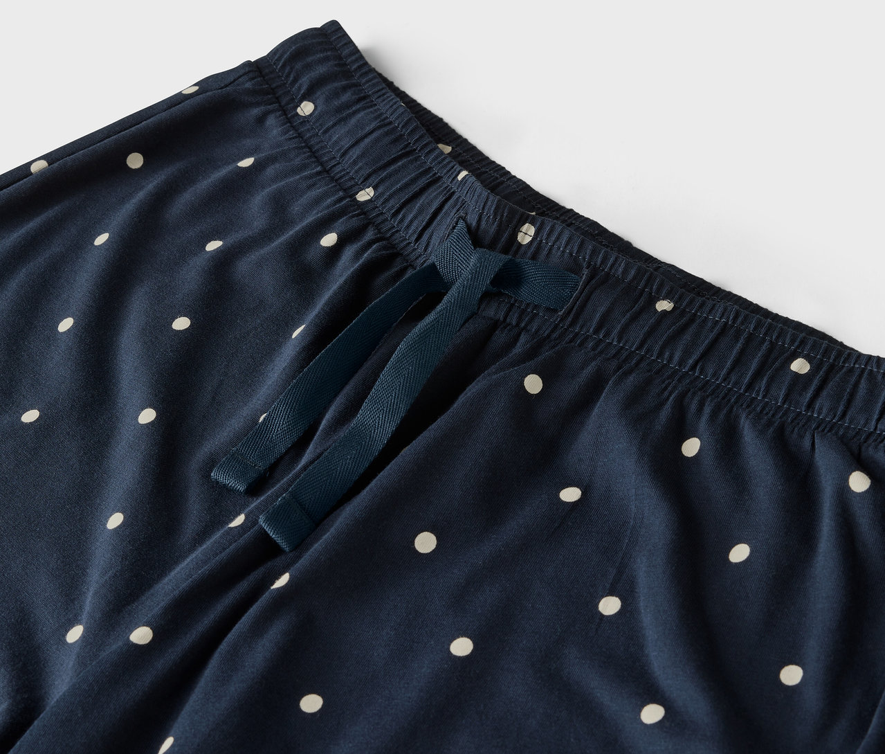 Egy sötétkék, fehér pöttyös nadrág részlete, gumis derékpánttal és húzózsinórral.