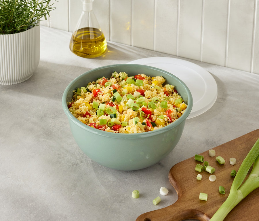 Zöld tál kuszkusszal és zöldségekkel, mellette hagyma egy vágódeszkán.