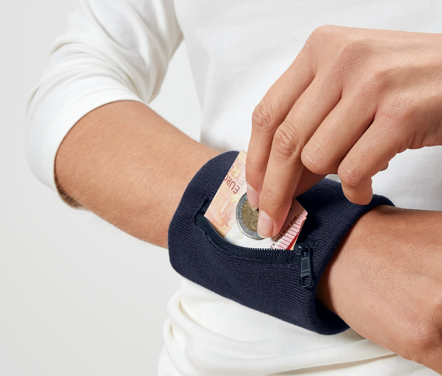 Egy személy euróérmét tesz egy tengerészkék színű csuklópénztárcába.