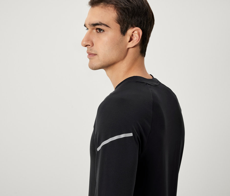 Férfi profilból, fekete, hosszú ujjú pólót visel fényvisszaverő csíkkal.