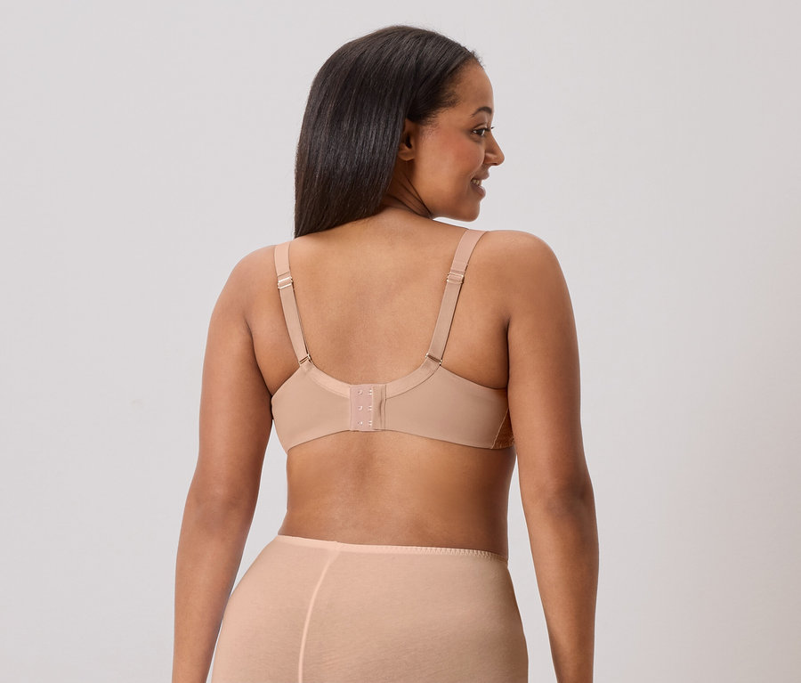 Hátulnézet egy hosszú, sötét hajú nőről, aki testszínű melltartót és hozzáillő alsóneműt visel.
