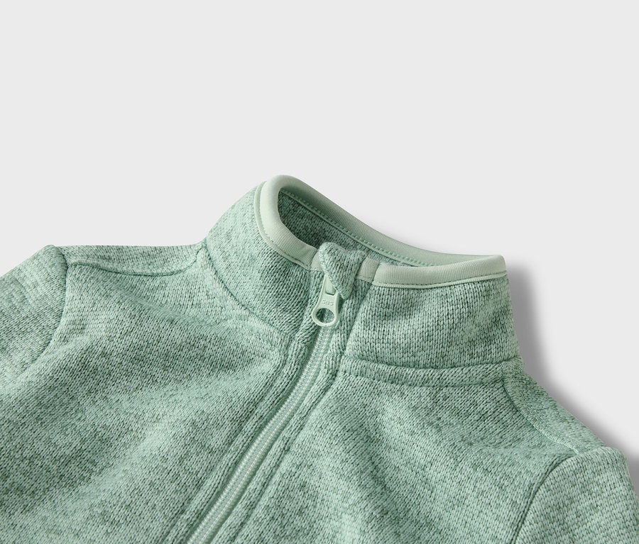 Egy világoszöld, cipzáras polár pulóver közeli képe.