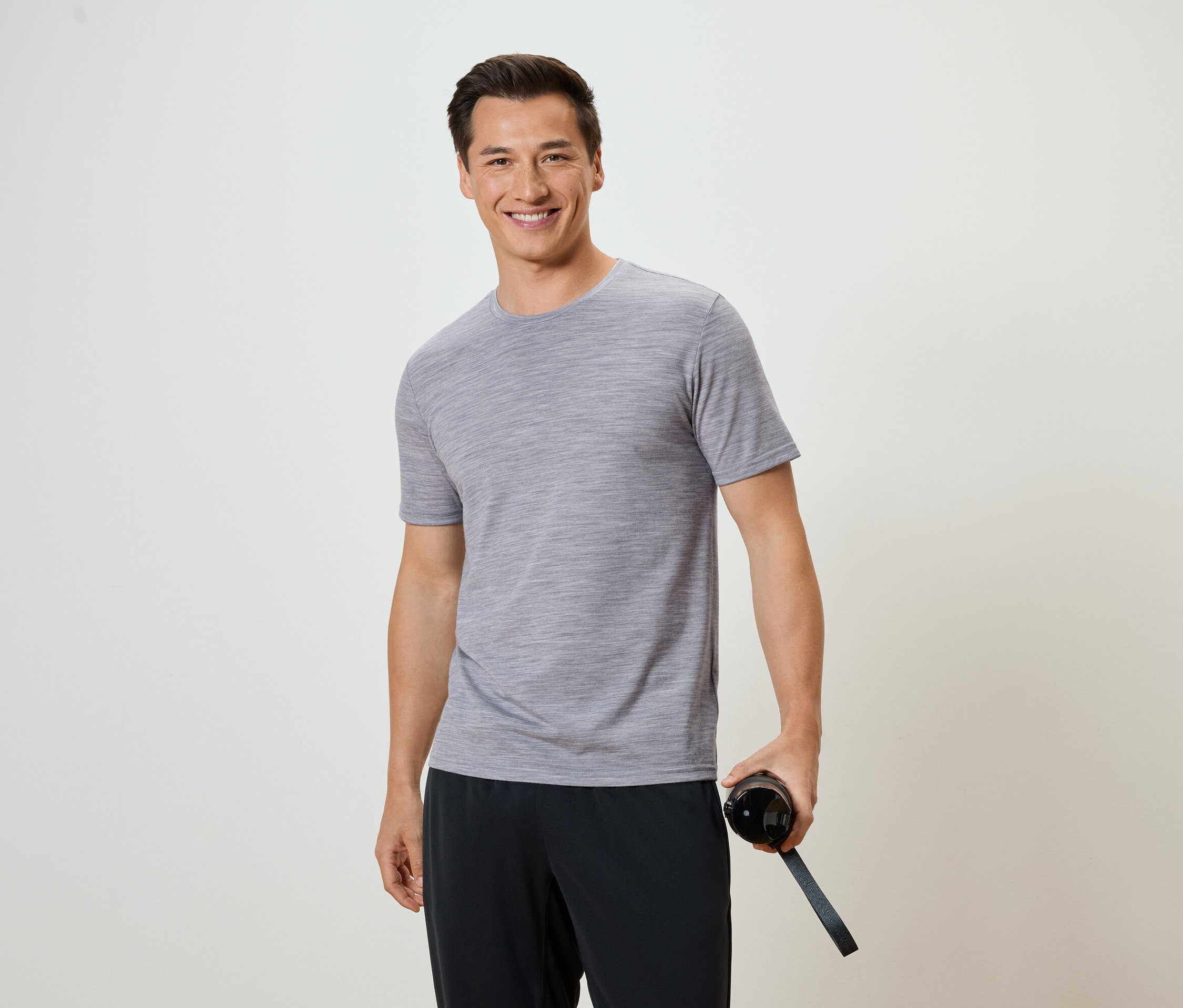 Férfi szürke pólóban és fekete nadrágban vizet tart.