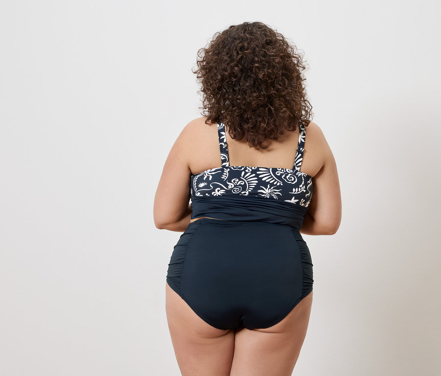 Hátulról látható egy göndör hajú nő, aki sötétkék, fehér mintás tankini felsőt és sötétkék, magas derekú bikini alsót visel.