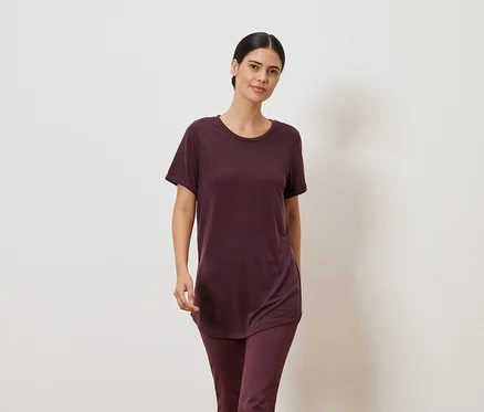 Bordó pólót és leggingset viselő nő semleges háttér előtt.