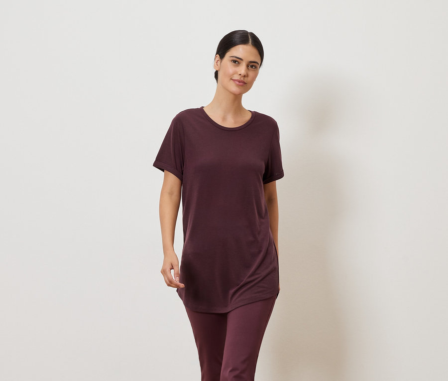 Bordó pólót és leggingset viselő nő semleges háttér előtt.