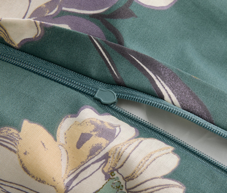 Közelkép egy cipzárról egy zöldes virágmintás anyagon.