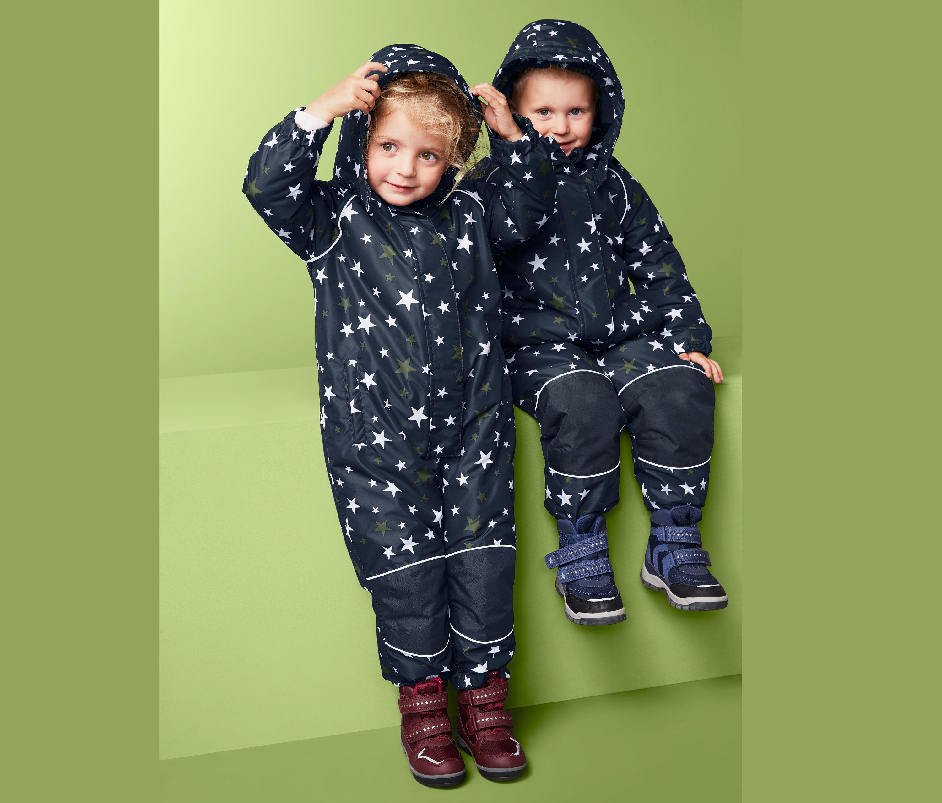 Csillagmintás téli kezeslábast viselő gyerekek ülnek egymás mellett.