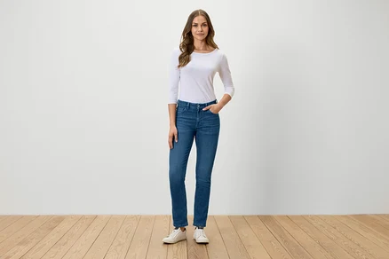 Frau steht und posiert in blauen Jeans, weißem T-Shirt und weißen Turnschuhen.