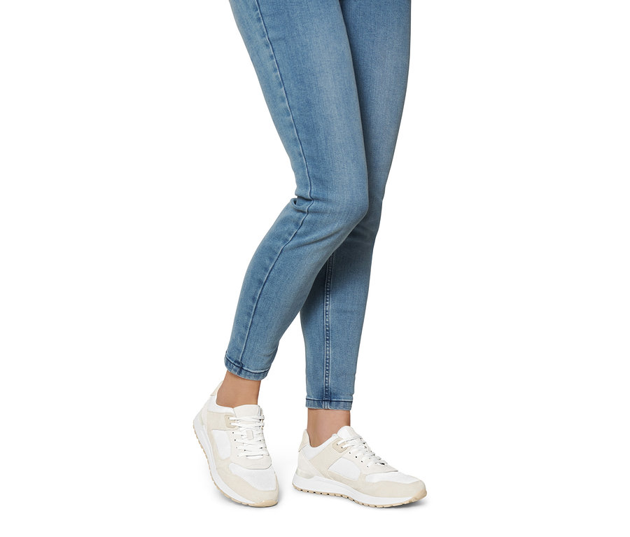 Egy nő lábai farmerben és krémszínű velúrbőr sneaker cipőben.