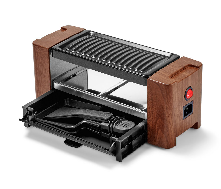 Közelkép egy kétszemélyes raclette-ről, kihúzott fiókkal és tartozékokkal.