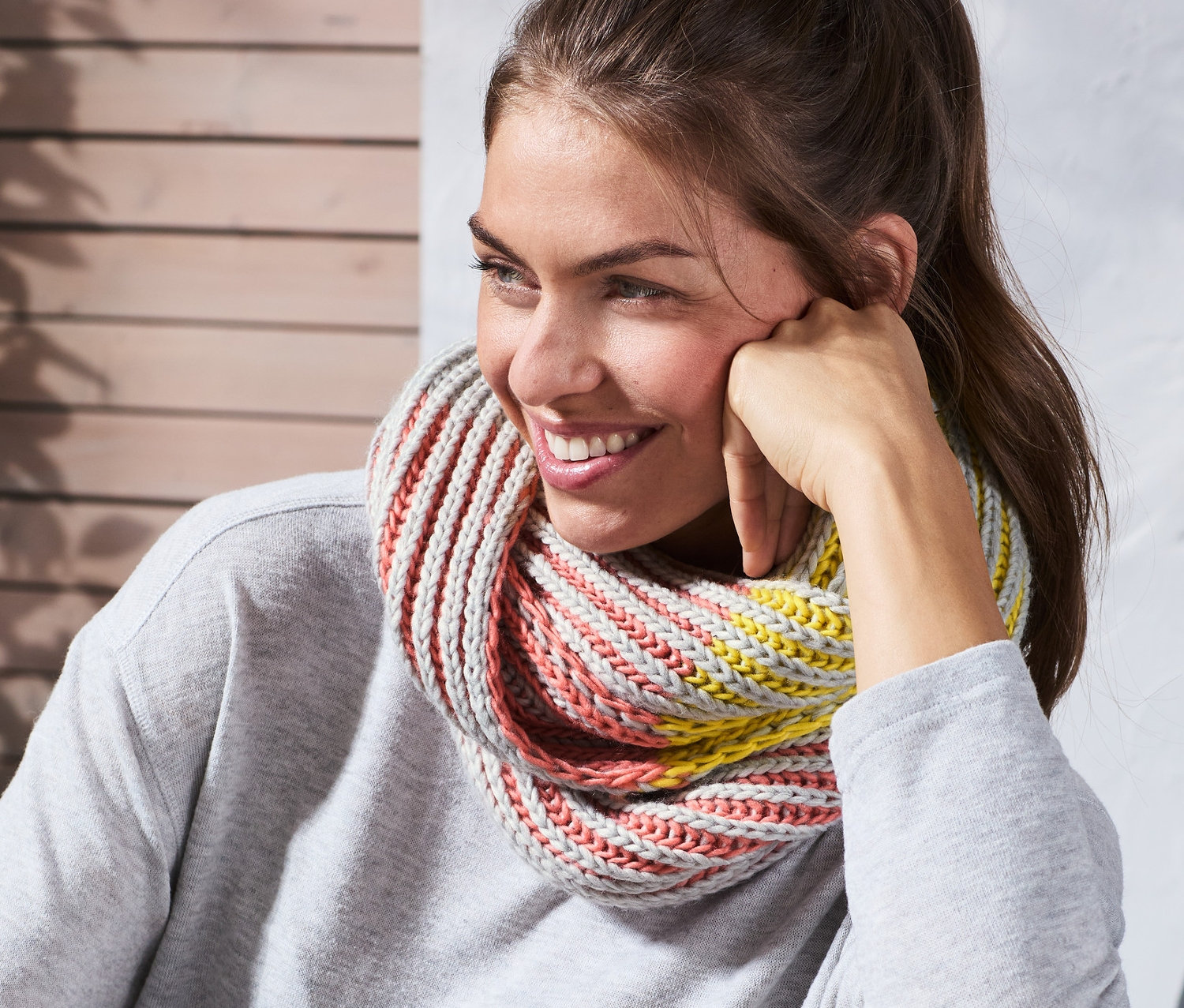 Mosolygó, copfos nő ül a szabadban, és színes kötött csősálat visel.