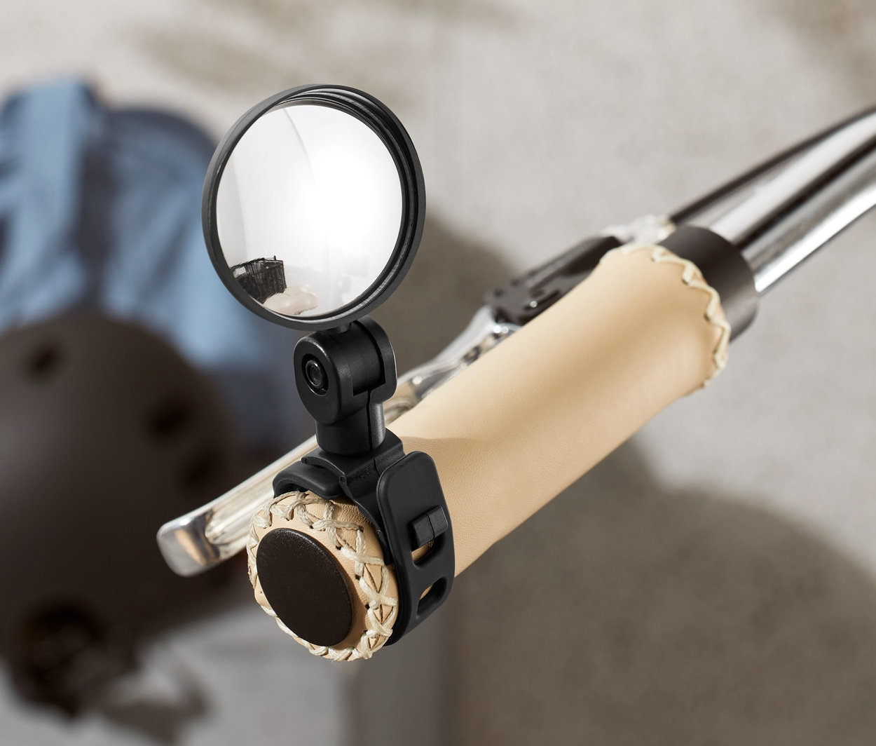 Egy kerékpár kormányának közeli képe, mini visszapillantó tükörrel. A háttérben sisak és kabát látható.